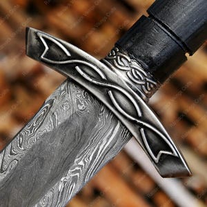 May include: Close-up of a sword with a patterned blade and a silver crossguard. The handle is black, and the blade has a distinctive wave-like pattern. The crossguard features an intricate design.