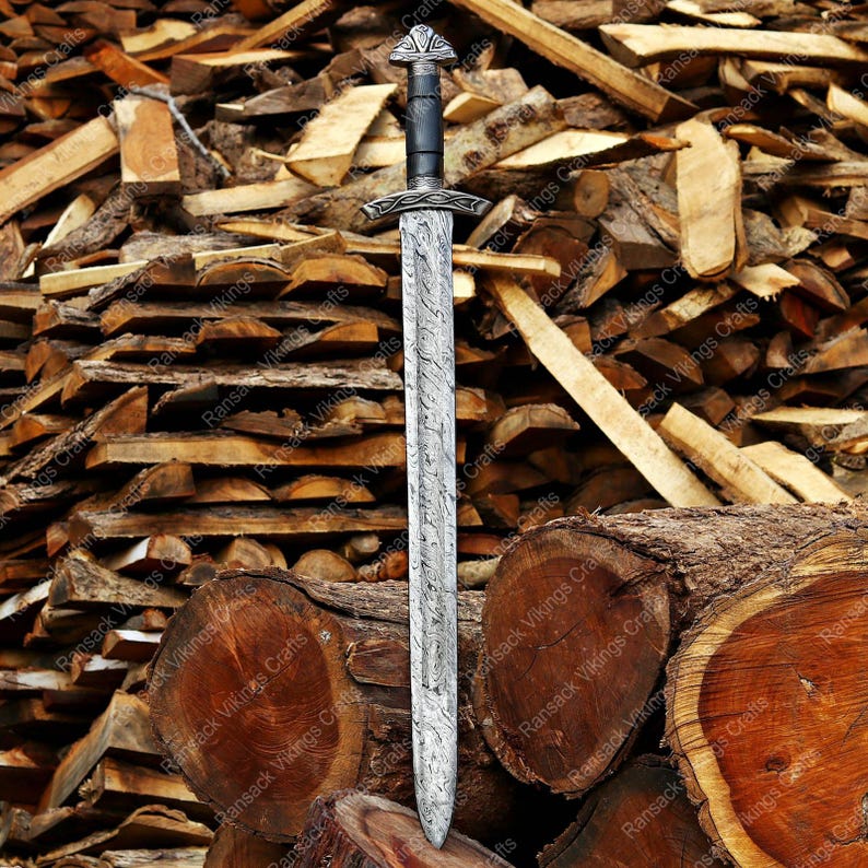 May include: A detailed image of a Viking sword with a silver blade and a black handle. The sword features intricate designs on the blade and hilt. The background is a pile of stacked wood logs, creating a rustic aesthetic.