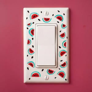 Op de afbeelding: Een witte lichtschakelaar cover versierd met een herhalend patroon van watermeloen schijfjes in rood, teal en zwart. De schakelaar cover is rechthoekig met een enkele tuimelschakelaar in het midden.