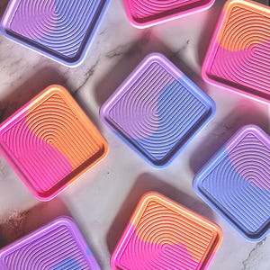 May include: A collection of square coasters featuring a raised, concentric arch pattern. Each coaster displays a vibrant colour-blocked design in combinations of bright pink, orange, and light purple, with smooth, rounded edges and a raised border.