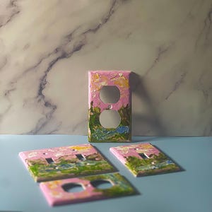 May include: Four rectangular electrical wall plates featuring a hand-painted landscape design with thick, textured brushstrokes in shades of pink, green, yellow, and blue. The plates include various configurations for toggle switches and duplex outlets.