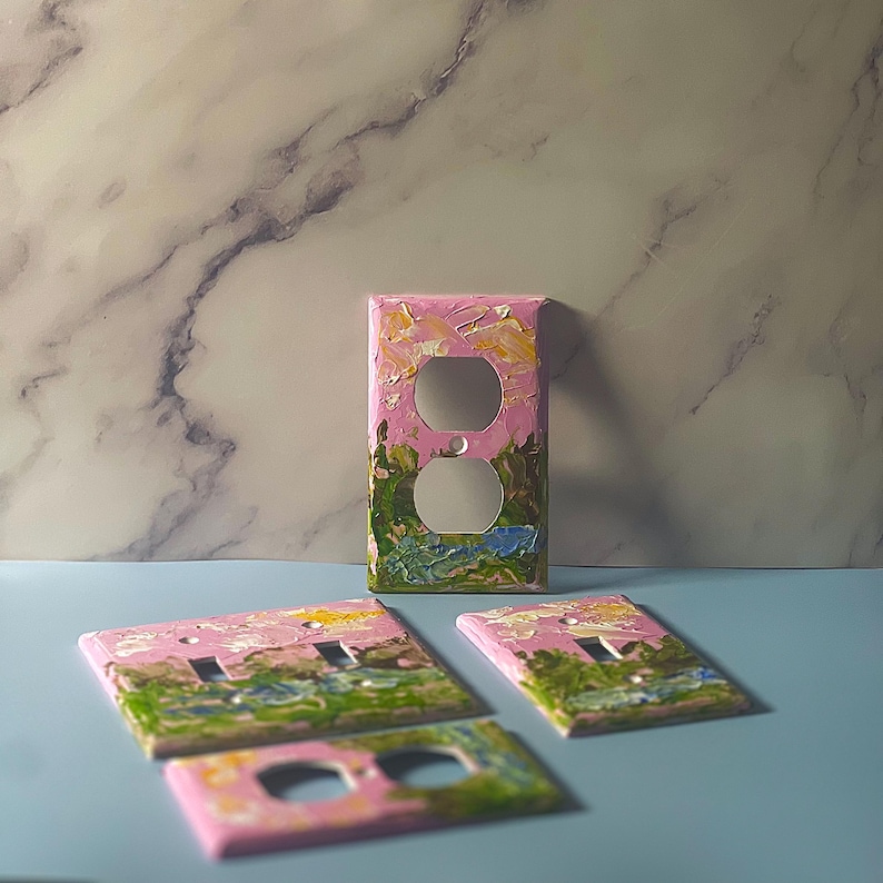 May include: Four rectangular electrical wall plates featuring a hand-painted landscape design with thick, textured brushstrokes in shades of pink, green, yellow, and blue. The plates include various configurations for toggle switches and duplex outlets.