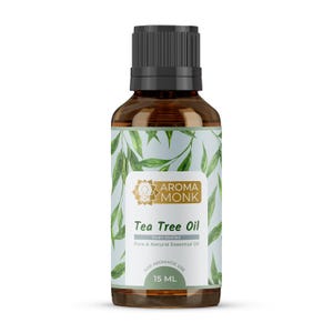 Könnte beinhalten: Aroma Monk Teebaumölflasche. Die bernsteinfarbene Glasflasche hat einen schwarzen Deckel und ein Etikett mit grünen Blätterillustrationen. Auf dem Etikett steht "Tea Tree Oil" und "15 ml".