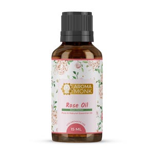 Op de afbeelding: Aroma Monk Rozenolie fles. De amberkleurige glazen fles heeft een zwarte dop en een etiket met bloemige rozenillustraties. Op het etiket staat "Rose Oil" en "Pure & Natural Essential Oil". De fles bevat 15 ml olie.