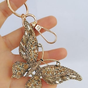 May include: Gold-toned butterfly keychain with clear and amber-colored crystals. The butterfly has detailed wings and a gold-colored metal frame. The keychain includes a split ring and a lobster clasp for easy attachment.