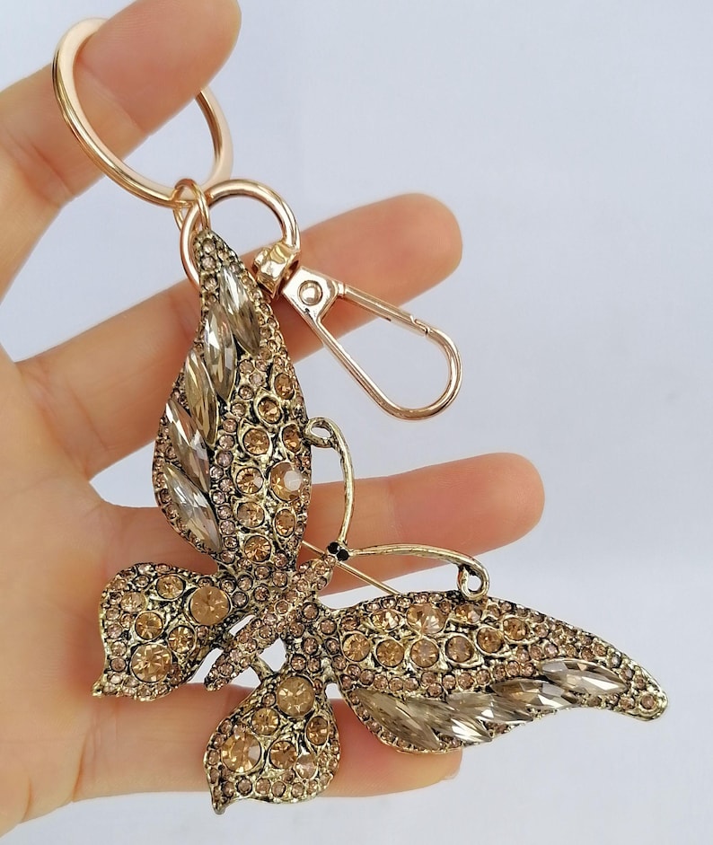 May include: Gold-toned butterfly keychain with clear and amber-colored crystals. The butterfly has detailed wings and a gold-colored metal frame. The keychain includes a split ring and a lobster clasp for easy attachment.