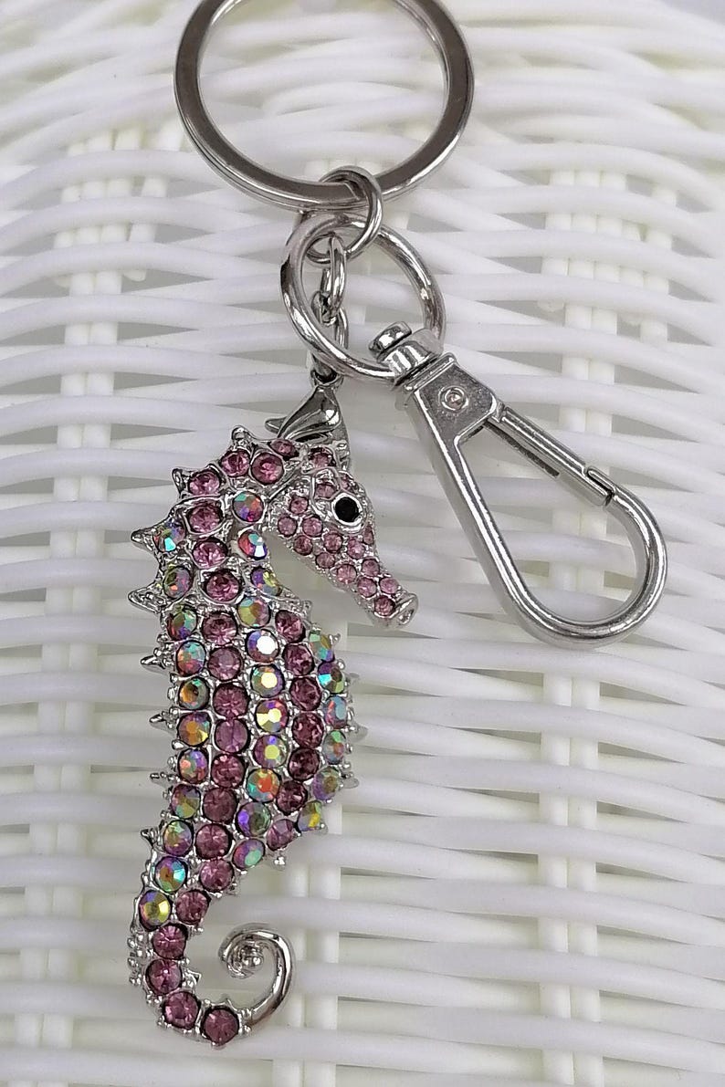 K&ouml;nnte beinhalten: Ein silberfarbener Seepferdchen-Schl&uuml;sselanh&auml;nger mit rosa und irisierenden Strasssteinen. Das Seepferdchen hat ein detailliertes Design mit einem Karabinerverschluss und einem Schl&uuml;sselring. Ein dekoratives Accessoire.