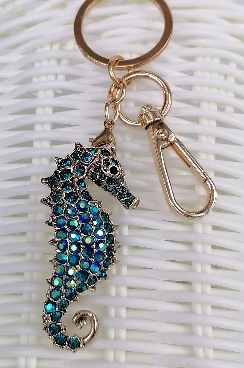 K&ouml;nnte beinhalten: Ein goldfarbener Seepferdchen-Schl&uuml;sselanh&auml;nger mit Karabinerverschluss. Das Seepferdchen ist mit blau-t&uuml;rkisen schillernden Kristallen besetzt. Der Schl&uuml;sselanh&auml;nger ist ein dekoratives Accessoire.