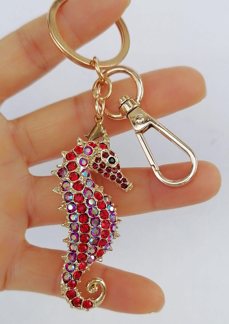 K&ouml;nnte beinhalten: Goldfarbener Seepferdchen-Schl&uuml;sselanh&auml;nger mit roten und irisierenden Strasssteinen. Der Seepferdchen-Anh&auml;nger ist mit einer goldenen Metalloberfl&auml;che und einem Karabinerhaken versehen. Ein dekoratives Accessoire.