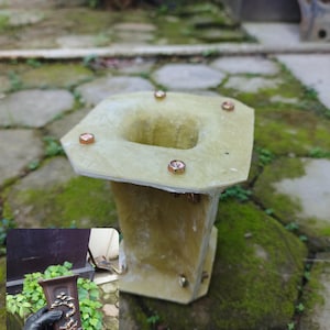 May include: A light yellow, rectangular planter with a square opening and copper-coloured accents. The planter is outdoors on a stone surface with moss. A smaller, brown bonsai pot is shown in the corner.