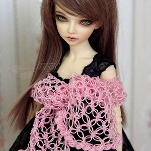Puede incluir: Una mu&ntilde;eca con el pelo largo y casta&ntilde;o que lleva un vestido negro con una chalina de ganchillo rosa.