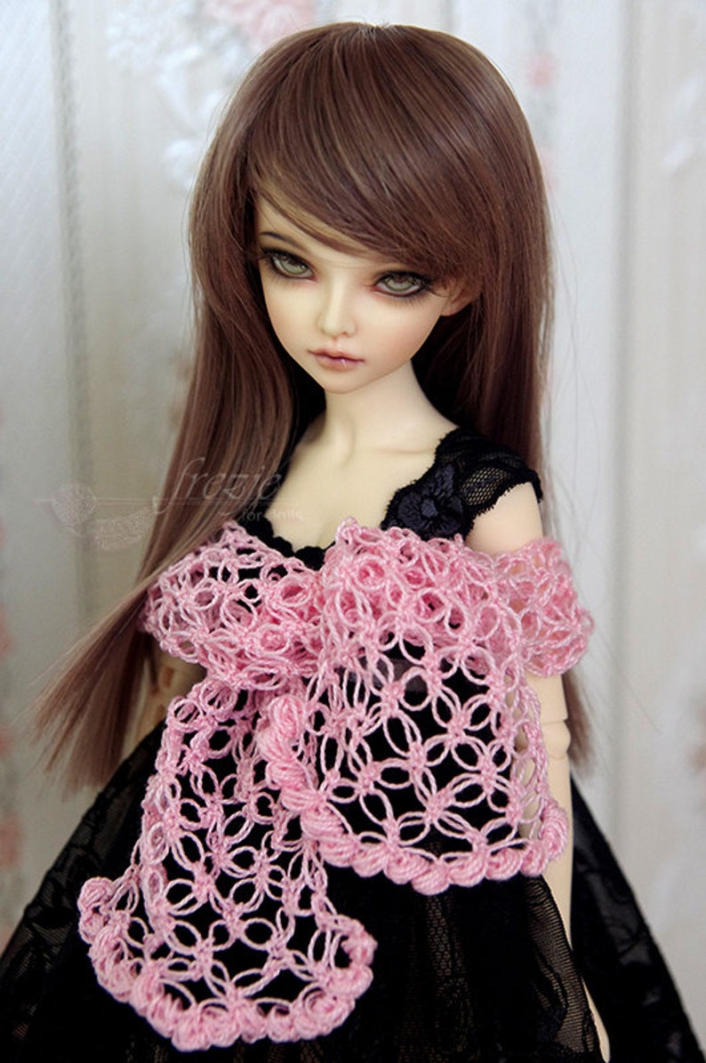 Puede incluir: Una mu&ntilde;eca con el pelo largo y casta&ntilde;o que lleva un vestido negro con una chalina de ganchillo rosa.