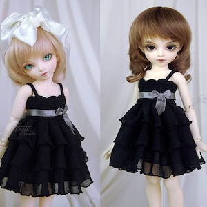 May include: Two dolls wearing black tiered dresses with a silver ribbon and bow. One doll has blonde hair with a white bow and the other doll has brown hair.