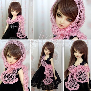 Puede incluir: Una bufanda de ganchillo rosa con un delicado patr&oacute;n floral. La bufanda est&aacute; drapeada alrededor de una mu&ntilde;eca con cabello casta&ntilde;o y un vestido negro.
