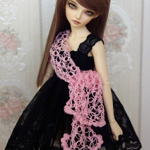 Puede incluir: Una mu&ntilde;eca con un vestido de encaje negro y una chalina de ganchillo rosa. La mu&ntilde;eca tiene el pelo largo y casta&ntilde;o y los ojos azules.