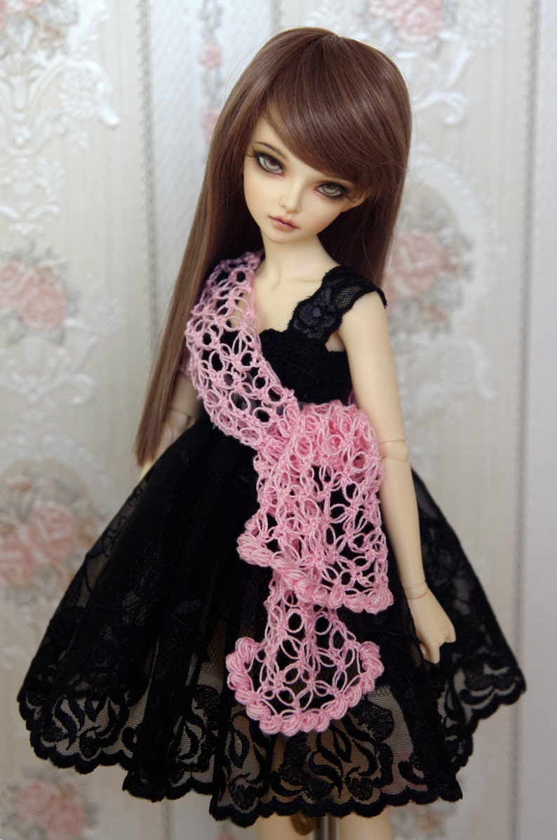 Puede incluir: Una mu&ntilde;eca con un vestido de encaje negro y una chalina de ganchillo rosa. La mu&ntilde;eca tiene el pelo largo y casta&ntilde;o y los ojos azules.