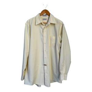 Op de afbeelding: Een lichtgele button-down shirt met lange mouwen, een borstzak en een kraag. Het shirt hangt aan een houten kleerhanger. De merknaam "L.L.Bean" is zichtbaar op het label.