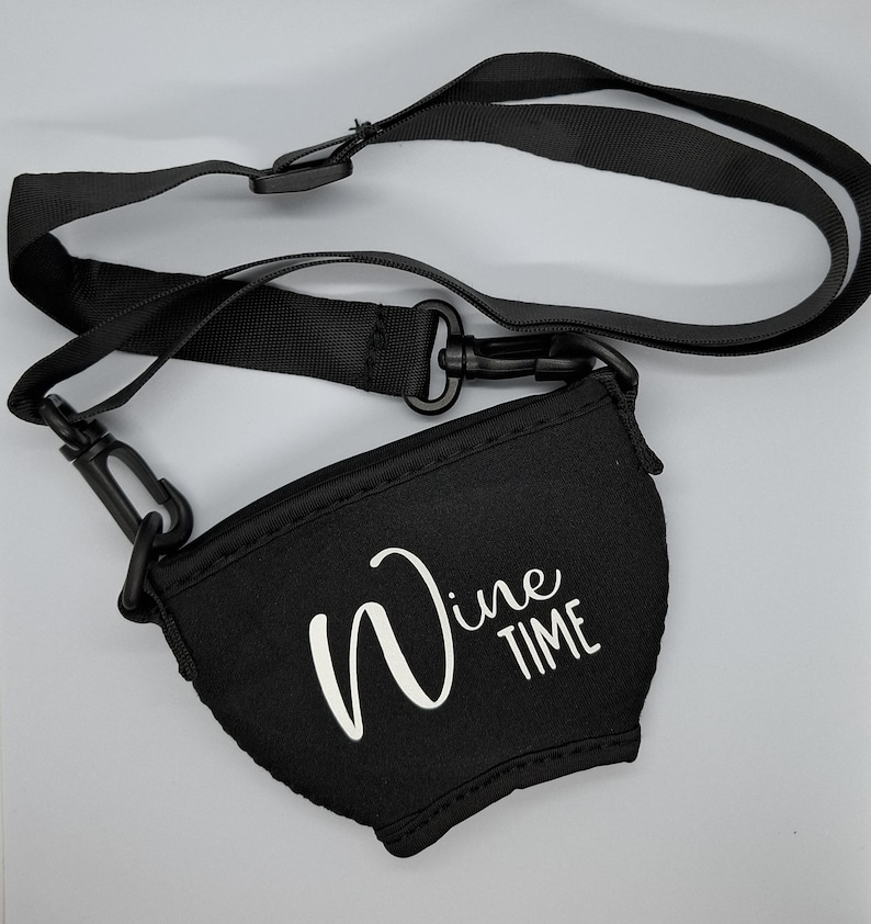 Ein schwarzer Weinglashalter mit einem schwarzen, verstellbaren Riemen und Clips. Auf dem Weinglashalter steht in weißer Schrift "Wine TIME".