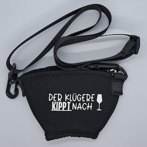 Schwarzer Neopren-Weinglashalter mit schwarzem Riemen und Clip. Der Halter hat weißen Text "DER KLÜGERE KIPPI NACH" und eine Weinglas-Grafik. Der Riemen ist verstellbar und kann um den Hals getragen werden.