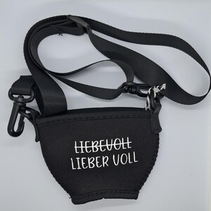 Schwarzer Weinglashalter mit verstellbarem schwarzem Riemen und schwarzem Kunststoffclip. Der Halter hat den weißen Text "LIEBEVOLL LIEBER VOLL".