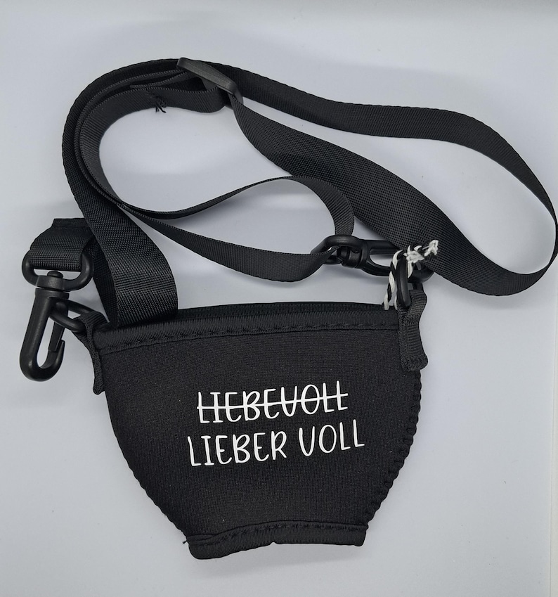 Schwarzer Weinglashalter mit verstellbarem schwarzem Riemen und schwarzem Kunststoffclip. Der Halter hat den weißen Text "LIEBEVOLL LIEBER VOLL".