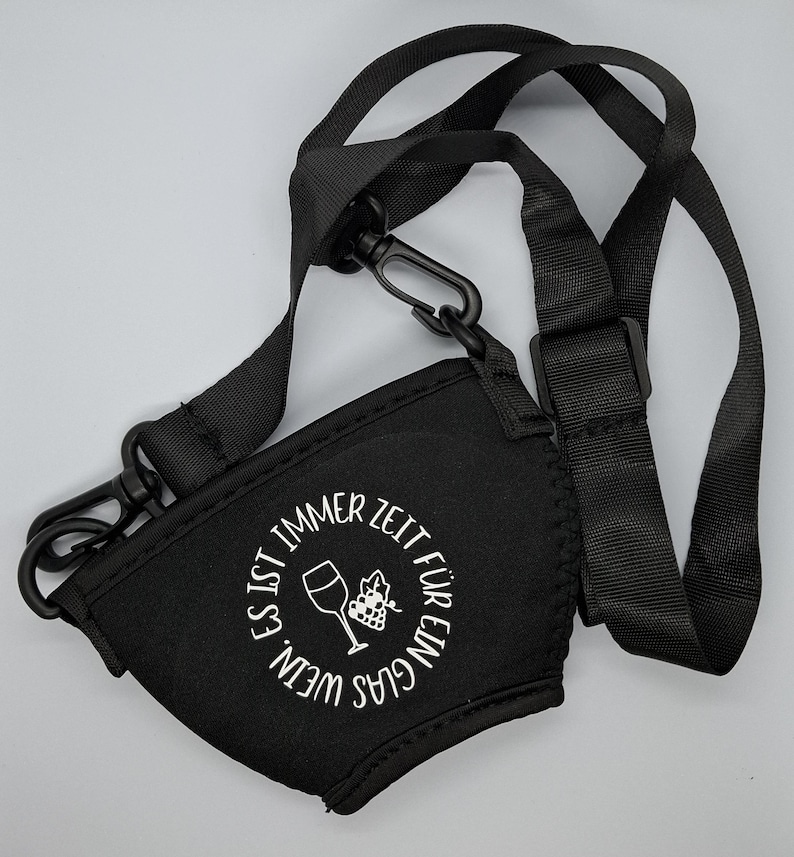 Schwarzer Weinglashalter mit schwarzem Riemen und Verschluss. Der Halter hat weißen Text mit der Aufschrift "WEIN. IST IMMER ZEIT FÜR EIN GLAS" um ein Weinglas und eine Trauben-Grafik.