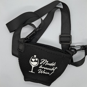 Schwarzer Weinglashalter mit einem schwarzen, verstellbaren Riemen. Der Halter hat den Text "Muddi braucht Wein!" und eine Weinglasgrafik mit Herzen. Der Halter ist für das Tragen eines Weinglases konzipiert.