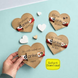 Op de afbeelding: Hartvormige kaarten van kraftpapier met Duitse tekst en een chocoladereep. De kaarten bevatten verschillende zinnen zoals 'Bedankt' en 'Voor jou'. Witte houten harten en een gele 'Direct downloaden'-sticker zijn ook aanwezig.