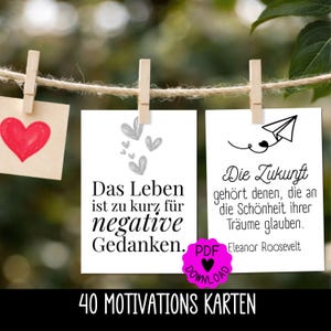 Könnte beinhalten: Drei Karten hängen an einer Schnur mit Wäscheklammern. Eine Karte hat ein rotes Herz, eine andere den Text "Das Leben ist zu kurz für negative Gedanken", und die dritte den Text "Die Zukunft gehört denen, die an die Schönheit ihrer Träume glauben."