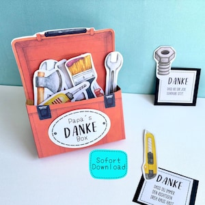 Könnte beinhalten: Eine orangefarbene Papier-Werkzeugkiste mit Werkzeugen wie Schraubenschlüssel und Pinsel. Auf der Werkzeugkiste steht "Papa's DANKE Box". Es gibt auch Karten mit dem Wort "DANKE" und einem Cutter.