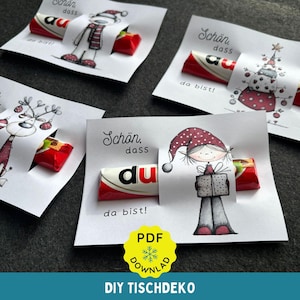 Könnte beinhalten: Vier weiße Geschenk-Anhänger mit Weihnachtsillustrationen, jeweils mit einem roten Schokoriegel. Die Anhänger tragen den deutschen Satz "Schön, dass du da bist!" und ein gelbes PDF-Download-Symbol.