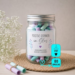 Könnte beinhalten: Ein klares Glasgefäß gefüllt mit gerollten pastellfarbenen Papierstreifen. Das Etikett trägt die Aufschrift "POSITIVE GEDANKEN im Glas" und "AFFIRMATIONEN FÜR MEHR SELBSTLIEBE & ACHTSAMKEIT". Zwei cyanfarbene Symbole zeigen "PDF" und "80 SPRÜCHE".