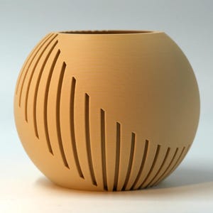 Op de afbeelding: Een bolvormige plantenbak met een matte lichtbruine afwerking, voorzien van een reeks verticale, gebogen uitsparingen die rond de zijkant lopen. Het object heeft een brede, ronde opening aan de bovenkant en een platte basis.