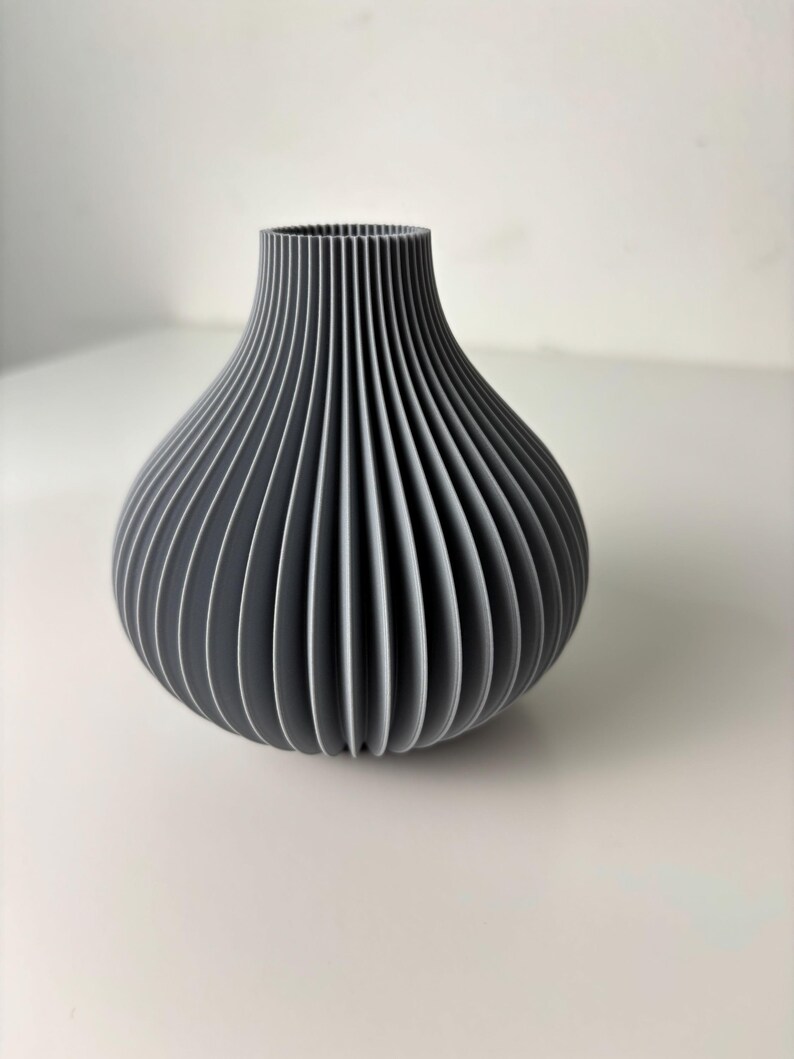 May include: A grey vase with a ribbed design. The vase has a bulbous body and a narrow neck. The vertical ribs create a textured surface. The vase is made of a solid material and is suitable for home decor.