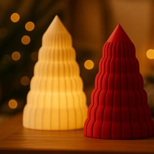 Könnte beinhalten: Zwei dekorative Objekte in Form eines Weihnachtsbaums. Eines ist warmweiß, das andere leuchtend rot. Beide haben ein gestuftes, geriffeltes Design und eine spitze Spitze. Sie stehen auf einer Holzoberfläche.