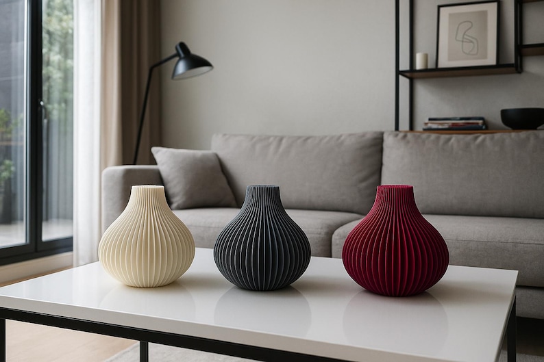 May include: Three decorative vases in cream, black, and burgundy, each with a ribbed, onion-shaped design. The vases are displayed on a white table in a living room setting. Home decor.