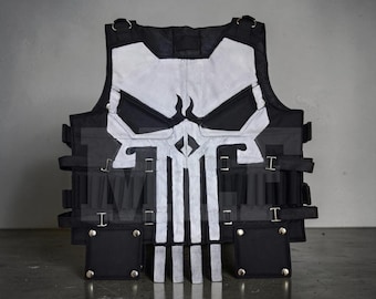 May include: A black tactical vest featuring a large, white, stylized skull graphic on the front. The vest includes multiple horizontal straps with metal buckles, two square pockets at the bottom with silver rivets, and D-ring attachments at the shoulders.