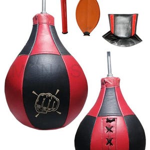 Puede incluir: Saco de velocidad rojo y negro en forma de lágrima con un gráfico de puño. Incluye una bomba de mano roja, una vejiga marrón y un protector de cuello negro y rojo. El texto en la parte superior dice: READY TO INSTALL FREE EXTRA BLADDER PROTECTION COVER.