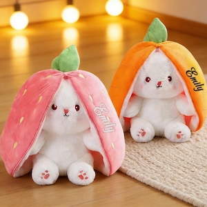 May include: Two plush bunny toys, one in a strawberry costume and the other in a carrot costume. The strawberry bunny is pink with yellow seeds, and the carrot bunny is orange. Both have the name "Emily" written on them.