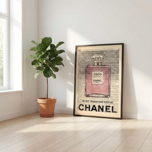 May include: Framed art print featuring a pink perfume bottle design with the text "COCO MADEMOISELLE CHANEL PARIS". The print is set against a vintage newspaper background, with the word "CHANEL" prominently displayed at the bottom.
