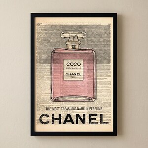 May include: A framed print featuring a pink perfume bottle design with the text "COCO MADEMOISELLE CHANEL PARIS." The print is set against a vintage newspaper background, with the word "CHANEL" prominently displayed at the bottom.