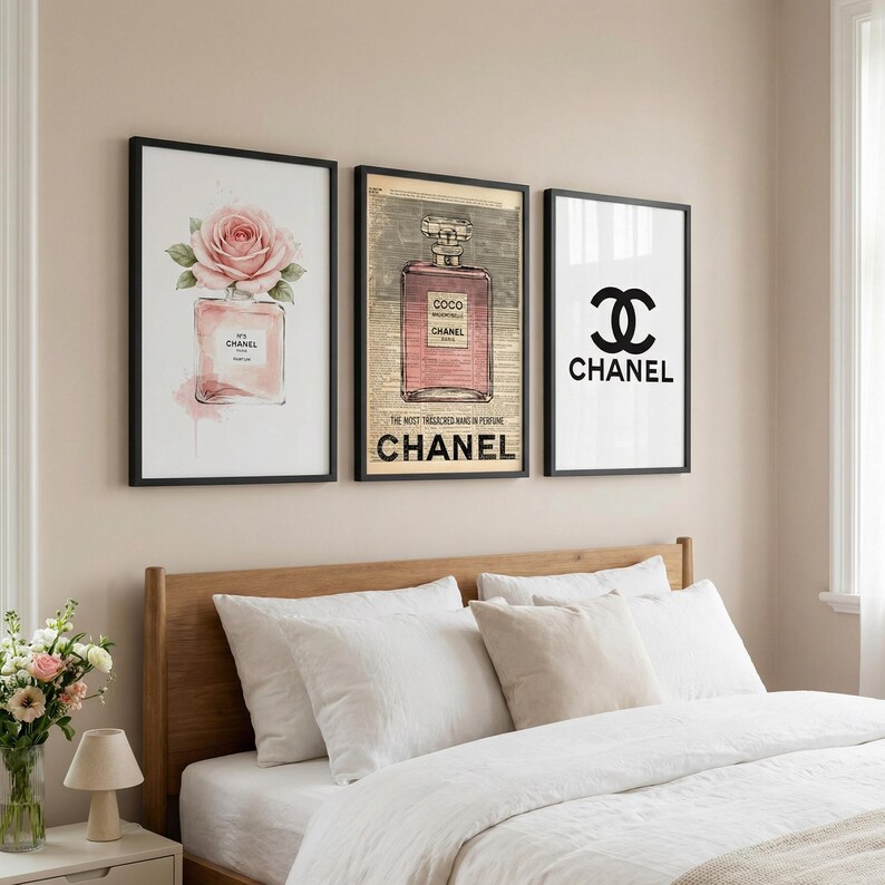 May include: Three framed prints with black borders. The prints feature Chanel-themed designs: a pink perfume bottle with a rose, a perfume bottle with text, and the Chanel logo. The prints are displayed above a bed.