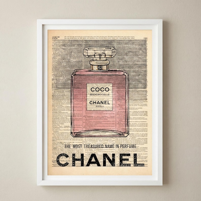May include: Framed print featuring a pink perfume bottle with the text "COCO MADEMOISELLE CHANEL PARIS" on a vintage newspaper background. The bottom of the print reads "THE MOST TREASURED NAME IN PERFUME" and "CHANEL".