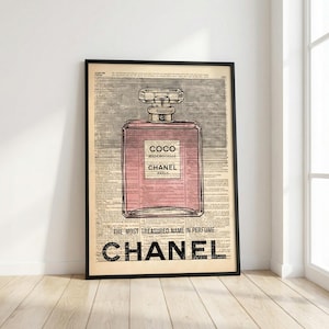 May include: Framed print featuring a pink perfume bottle design with the text "COCO MADEMOISELLE CHANEL PARIS." The print is set against a vintage newspaper background, with the words "THE MOST TREASURED NAME IN PERFUME" and "CHANEL" at the bottom.