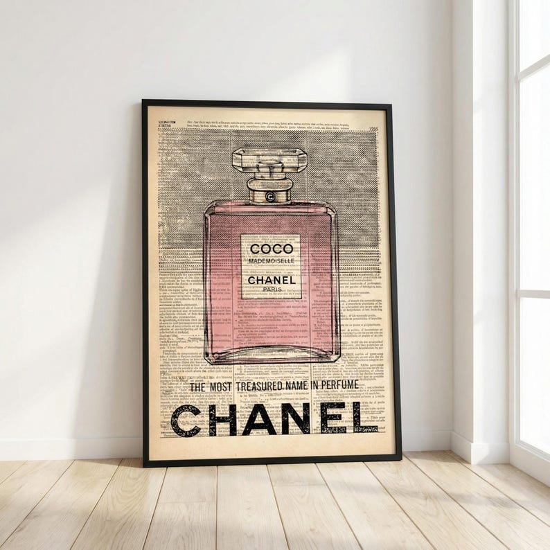 May include: Framed print featuring a pink perfume bottle design with the text "COCO MADEMOISELLE CHANEL PARIS." The print is set against a vintage newspaper background, with the words "THE MOST TREASURED NAME IN PERFUME" and "CHANEL" at the bottom.