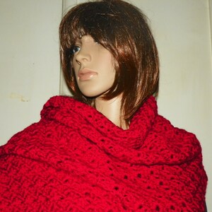 May include: A vibrant red, chunky-knit shawl draped over a mannequin. The shawl features a textured pattern and a wide, cowl-like collar. The bright red color is eye-catching, and the knit appears soft and warm. This accessory is perfect for adding a pop of color.