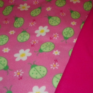 Manta de bebé de mariquitas verdes con un forro polar doble de color rosa fuerte cosido juntos