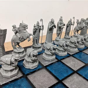 May include: A complete chess set with gray pieces on a blue and gray checkered board. The pieces include a rook, knight on horseback, bishop, queen, king, and pawns. The chess set is designed with a medieval theme.
