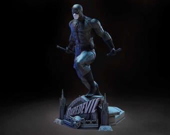 Puede incluir: Estatua detallada de Daredevil, el superhéroe de Marvel Comics, en una pose dinámica, sosteniendo bastones. La figura es predominantemente gris y azul, de pie sobre una base con el logo de Daredevil. La estatua tiene un diseño detallado y un fondo oscuro.