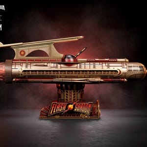 May include: A detailed model of a Flash Gordon spaceship, predominantly gold and red, with intricate detailing. The model is mounted on a decorative base with the Flash Gordon logo. The image includes text indicating a 50cm scale.